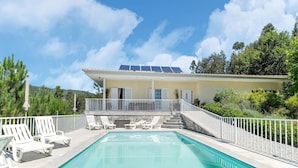 Un espace piscine avec une piscine à l’eau d’un bleu limpide, des chaises longues blanches et, au fond, un bâtiment équipé de panneaux solaires.