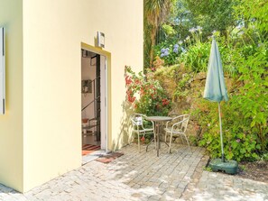 A patio with a table and chairs, a small umbrella, and a stone wall with plants. - Forest Hideaway Near Douro Valley (Abragão-Penafiel)
