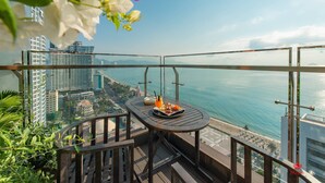 A balcony with a table set for two, overlooking a coastal cityscape with buildings and a beach. - Maple Hotel & Apartment (Nha Trang)