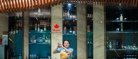 Zona de bar con estantes llenos de botellas y vasos, techo de madera y un letrero con una hoja de arce.