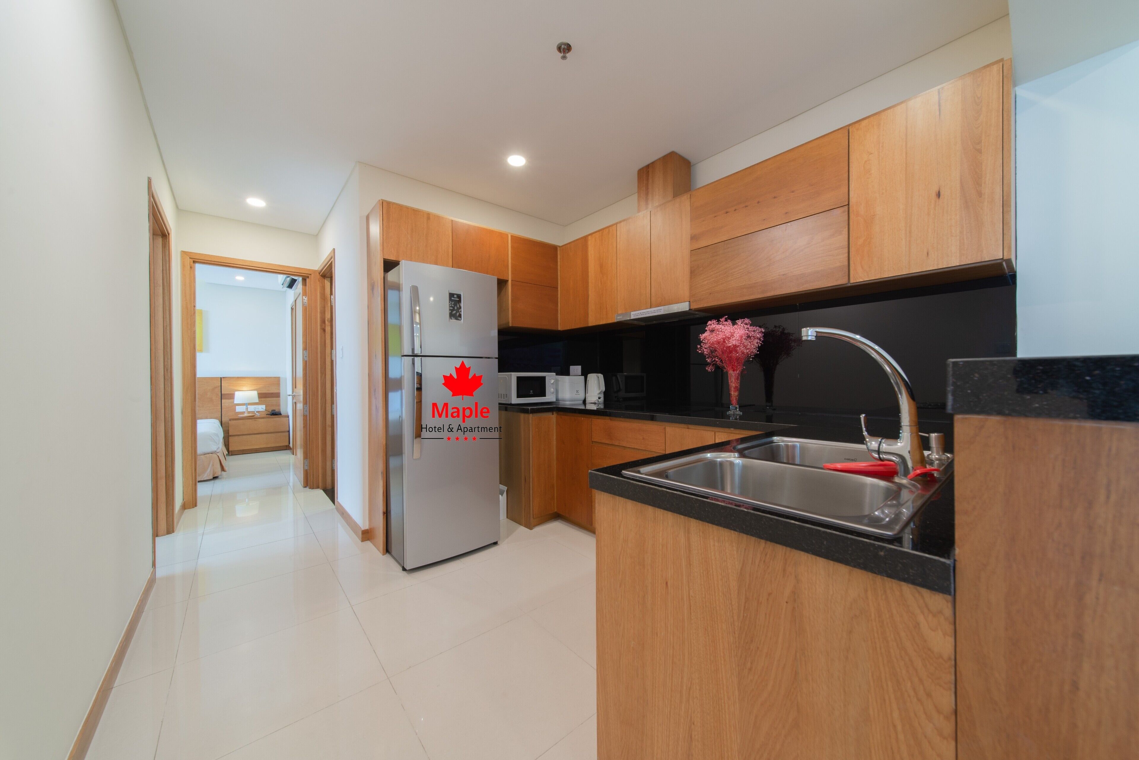 A modern kitchen with wooden cabinets, a stainless steel refrigerator, a microwave, and a sink with a red faucet.