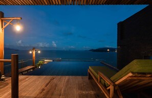 A wooden deck with a pool, lounge chairs, and a view of the sea at dusk. - Maple Hotel & Apartment (Nha Trang)