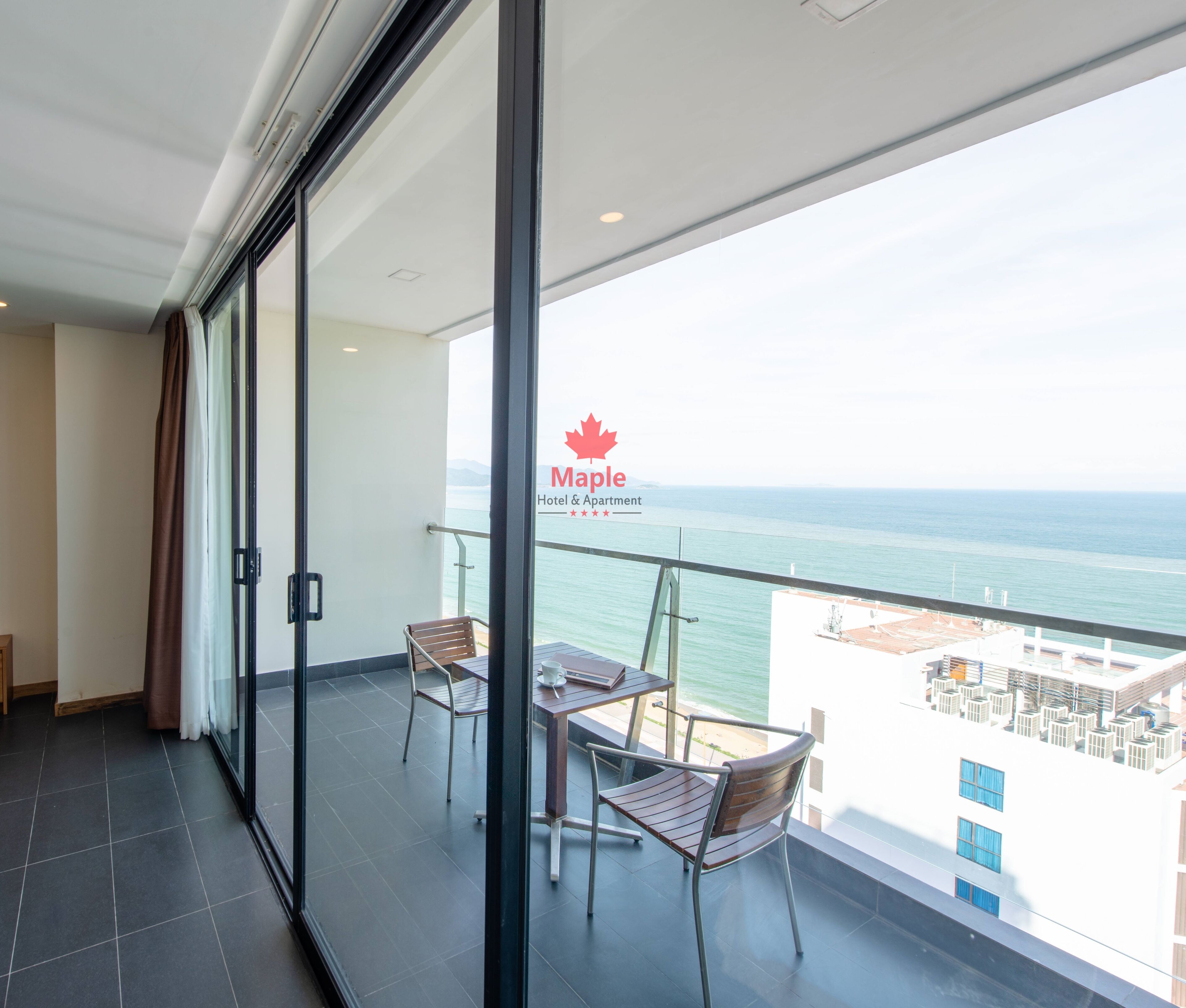 Een balkon met een glazen deur, twee stoelen en een tafel. Het logo van Maple Hotel & Apartment is zichtbaar op het glas.