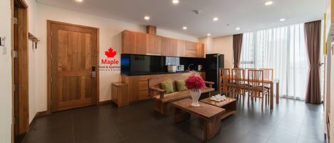 Une chambre d’hôtel moderne dotée d’une porte en bois, d’une kitchenette, d’un coin repas avec une table et des chaises, et d’une grande fenêtre avec des rideaux.