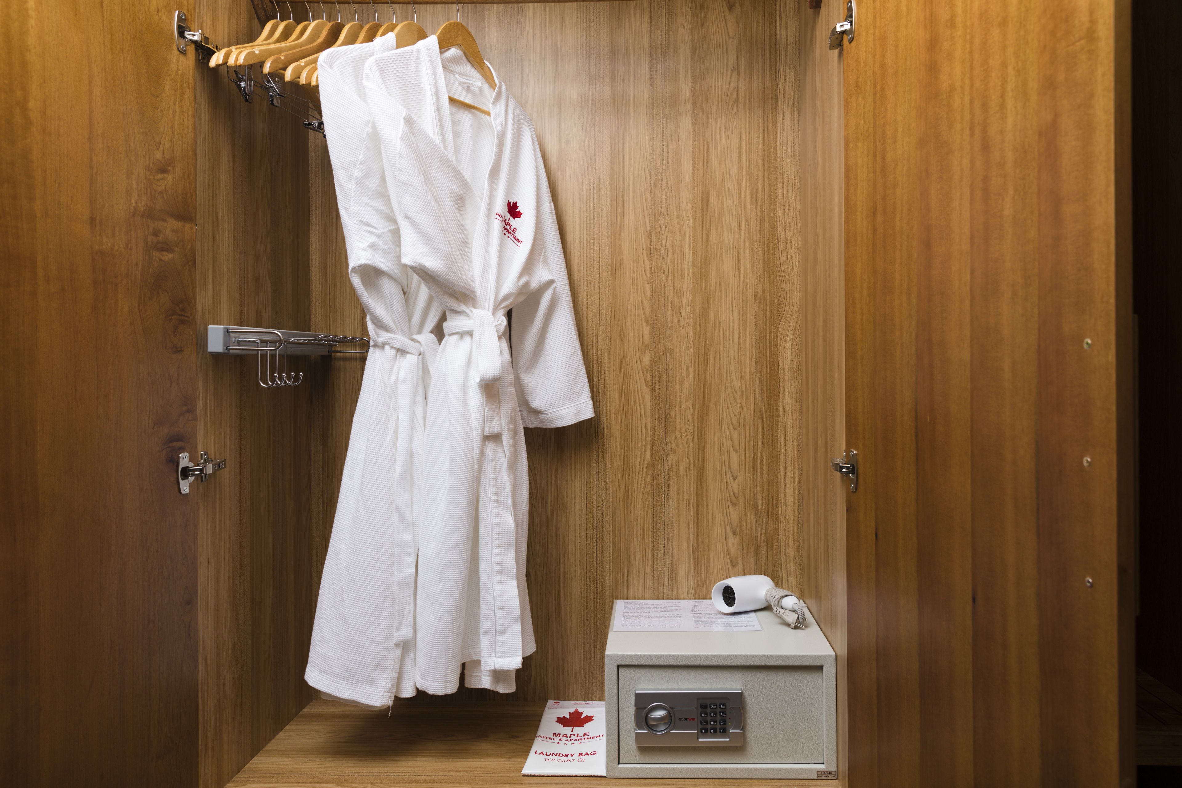 Een houten garderobe met een witte badjas die aan een rek hangt, een kleine witte doos met een haardroger, en een papieren handdoek op de vloer.