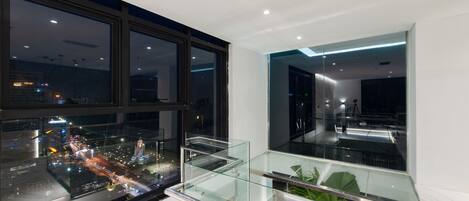 A modern interior with large windows, a glass railing, and a view of a cityscape at night.
