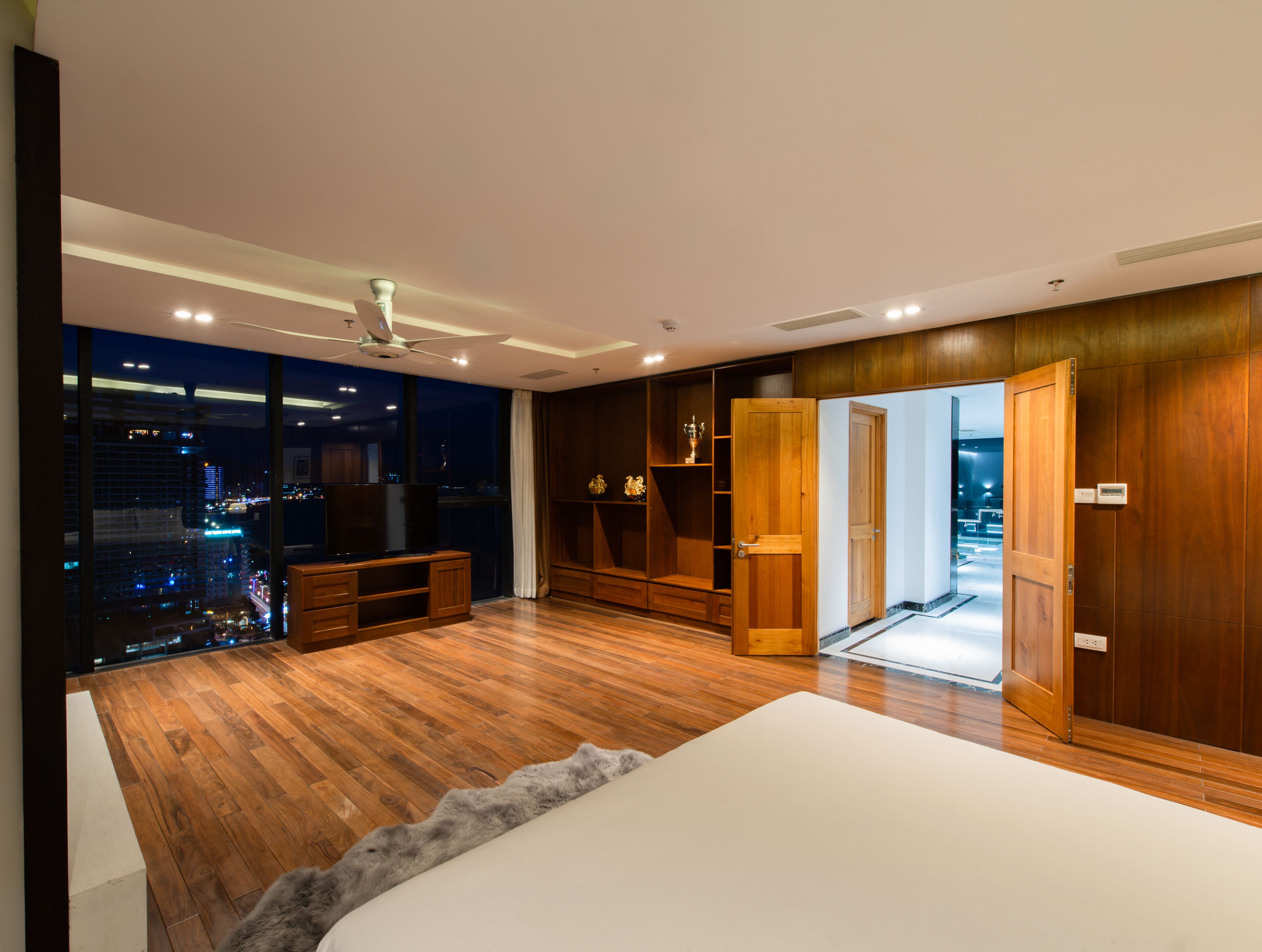 Ein modernes Schlafzimmer mit einem großen Bett, Holzboden, Blick auf die Stadt, Deckenventilator und integrierten Regalen.