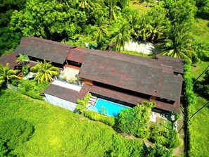 A large, two-story house with a swimming pool, surrounded by lush greenery and palm trees. - Gili Buana Hostel & Backpackers (Gili Air)