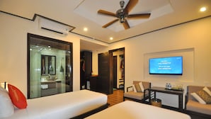 A hotel room with two beds, a television, a ceiling fan, and a bathroom visible through a glass door. - The Quin Riverside Villa (Da Nang)