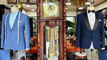 A room with a large wooden grandfather clock, two mannequins dressed in suits, and a ceiling fan.