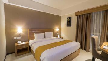 A hotel room with a large bed, bedside tables with lamps, a desk, and a view of the city through the window.