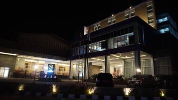 A modern building with a glass facade, a visible entrance, and a parking area with cars.