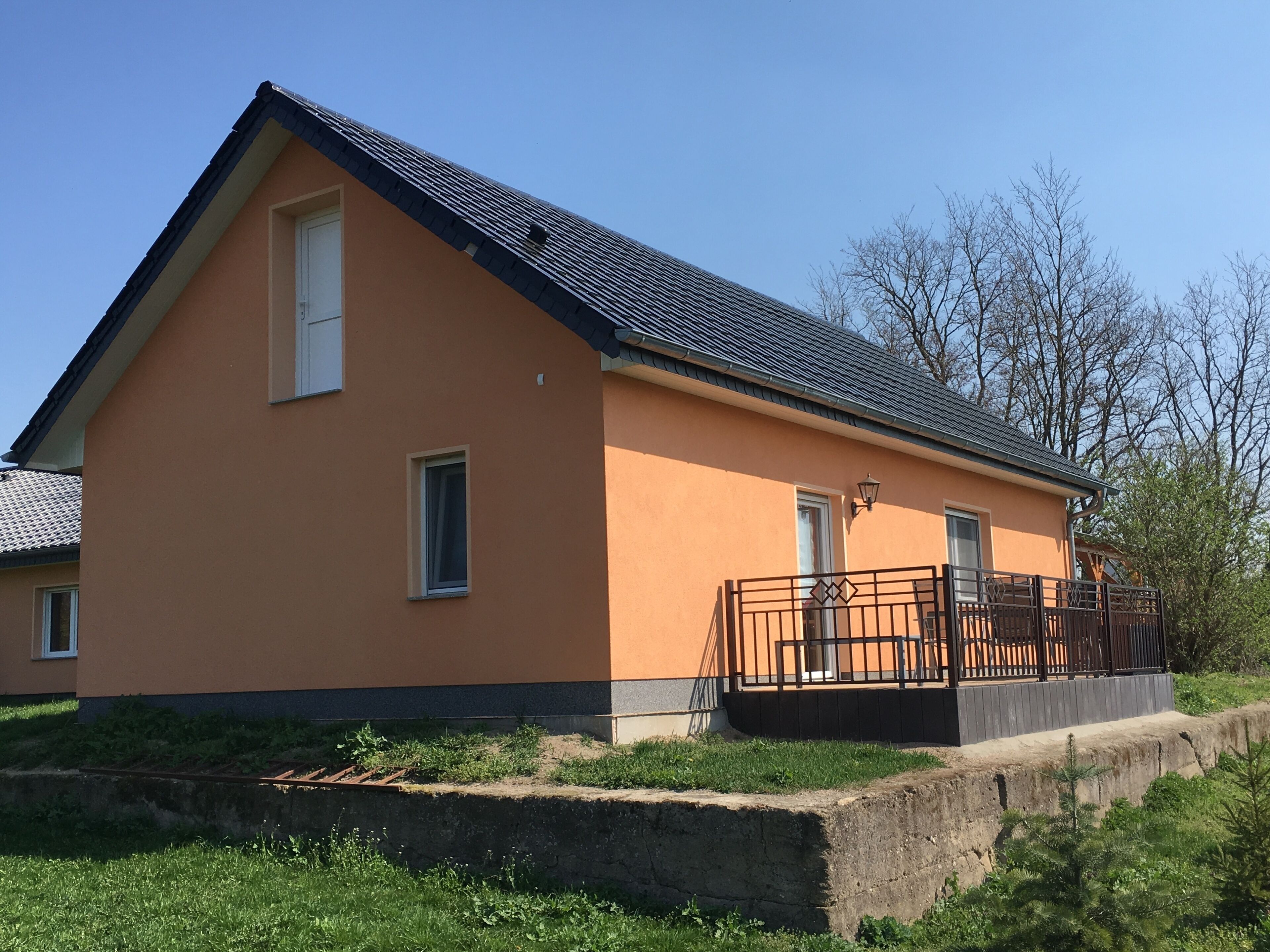 Een huis met twee verdiepingen, een schuin dak, een balkon met metalen hekwerk en een klein portaaltje.