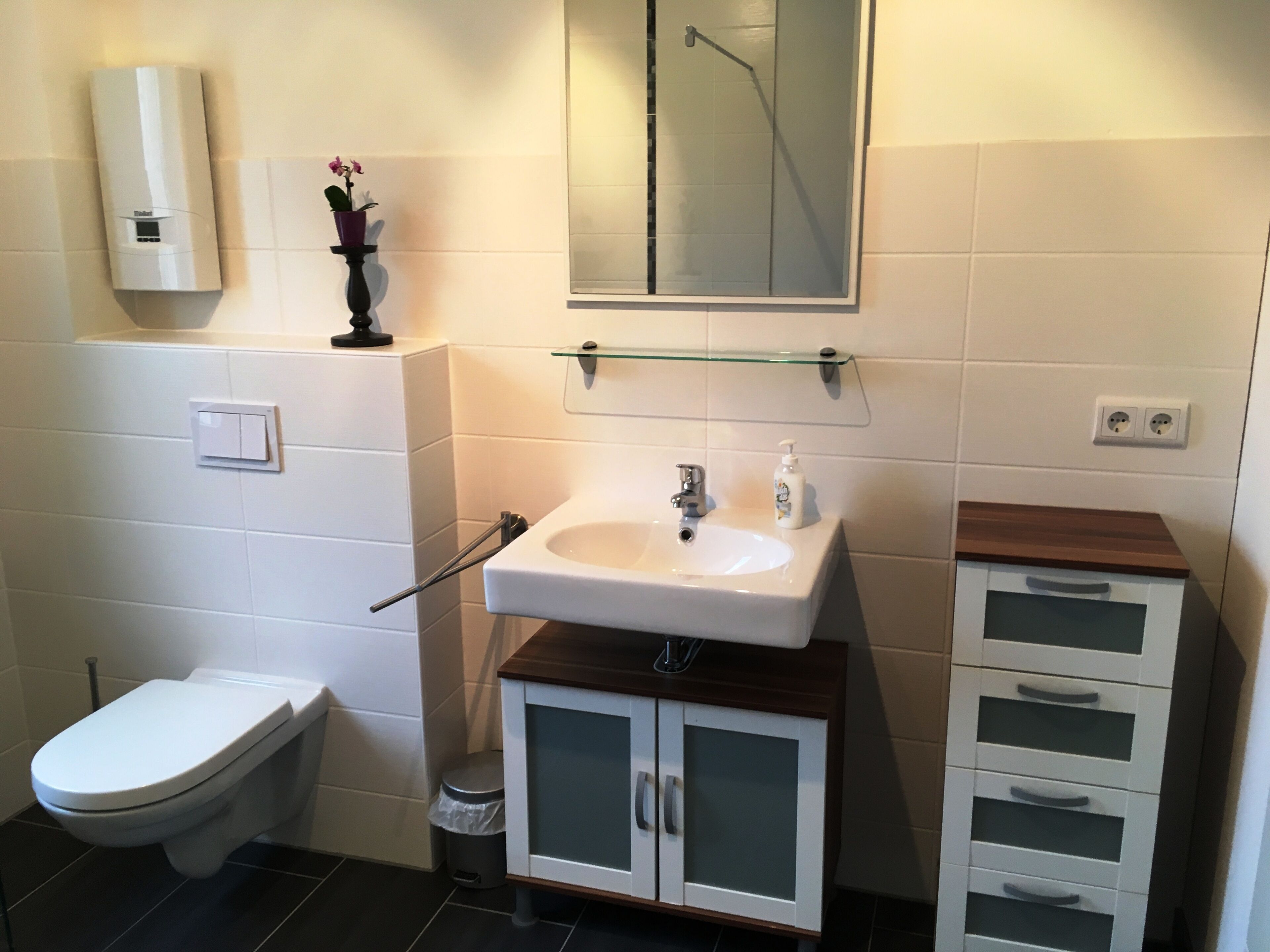 A bathroom with a toilet, sink, mirror, and cabinet.