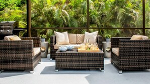 A balcony with wicker furniture, a grill, and lush greenery in the background.
