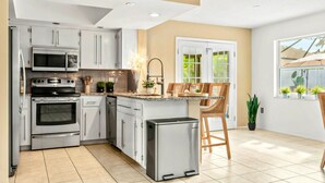 A modern kitchen with stainless steel appliances, white cabinets, and a small refrigerator.