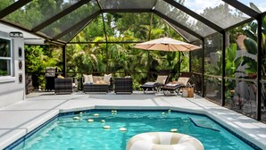An indoor swimming pool with clear water, surrounded by lounge chairs and a glass enclosure.
