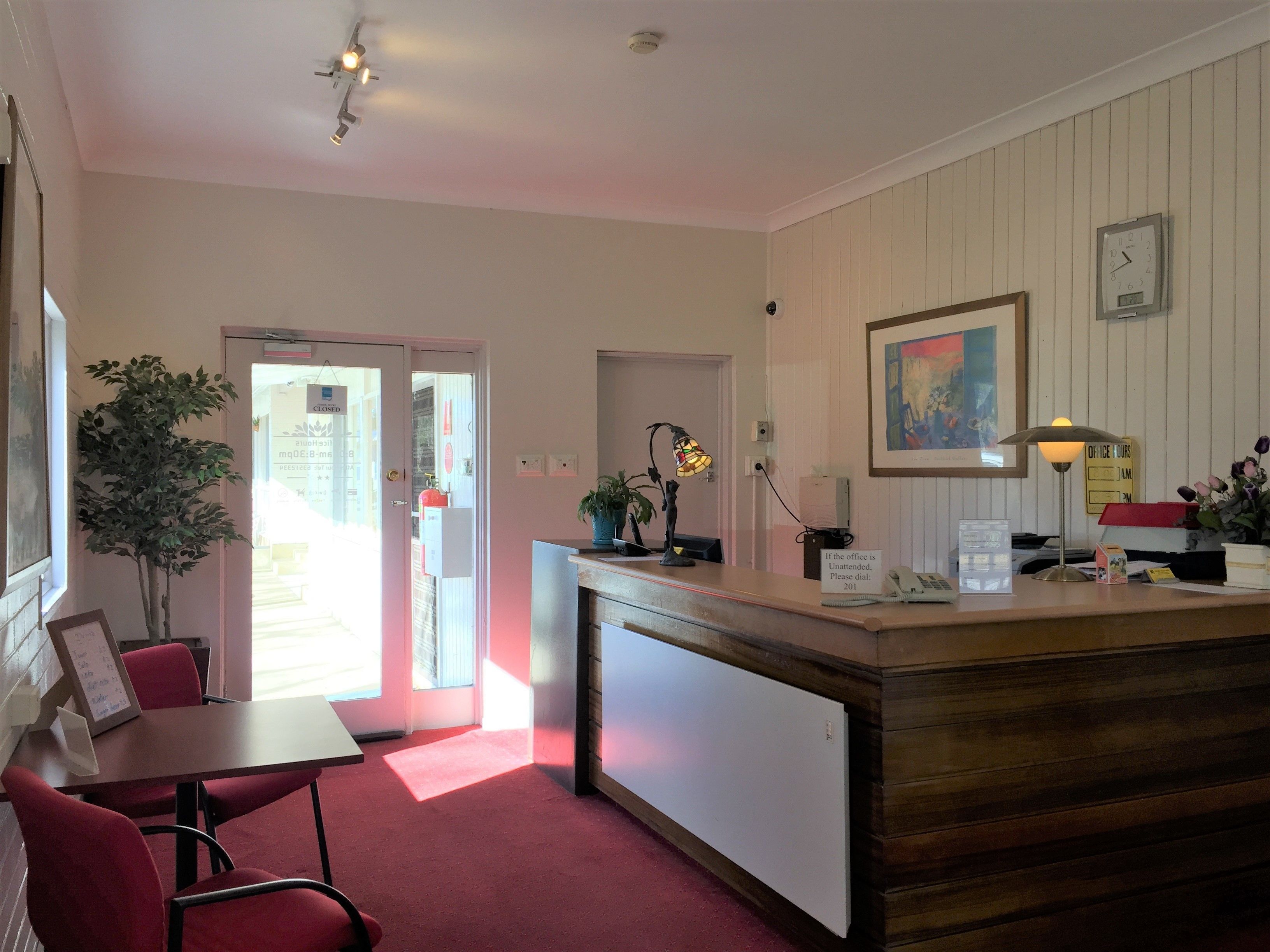 A reception area with a desk, a telephone, a clock, and a framed painting on the wall.