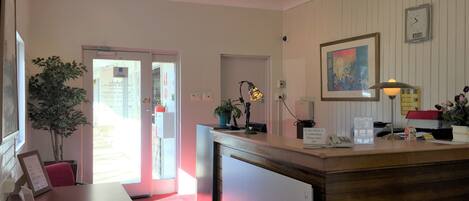 A reception area with a desk, a telephone, a clock, and a framed painting on the wall.