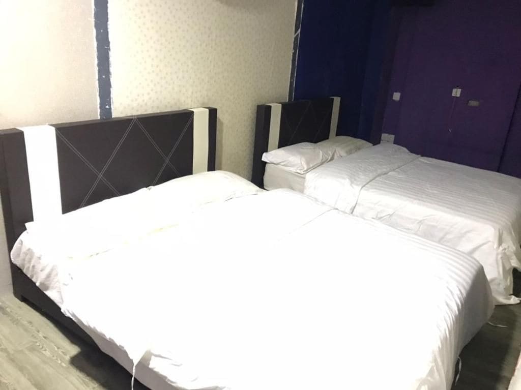 A hotel room with two beds, a large window, and a blue wall.