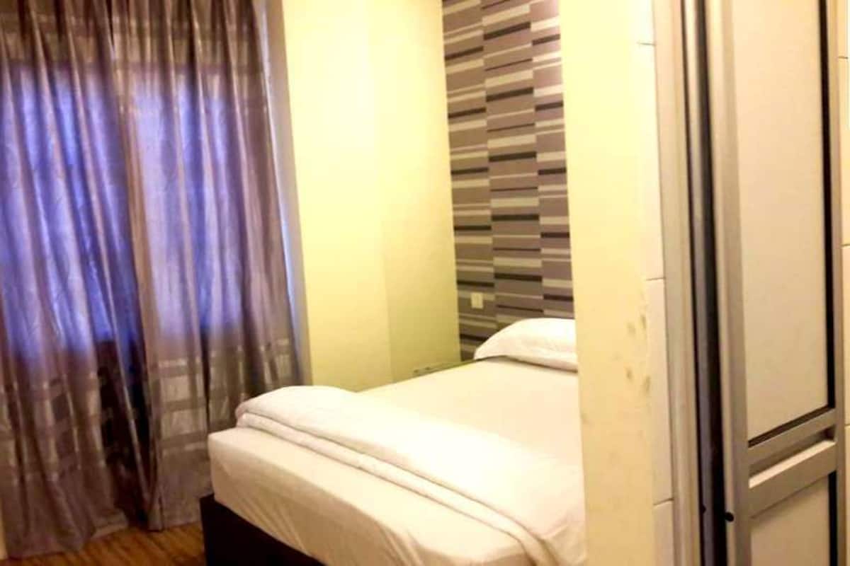 Una cama pequeña y bien hecha en una habitación con pared a rayas y una cortina.