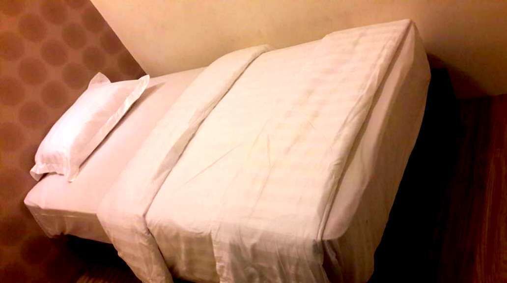 Un lit avec du linge de lit blanc, un plancher en bois et un mur orné de motifs.