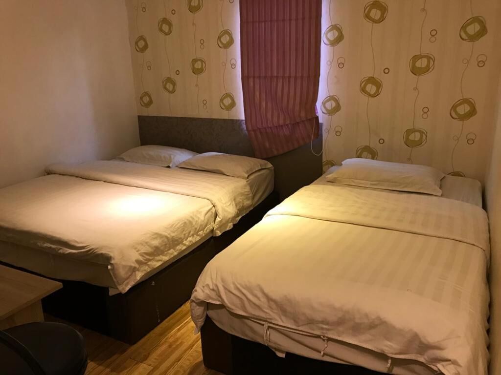 A room with two single beds, a wooden floor, and a window with a curtain.