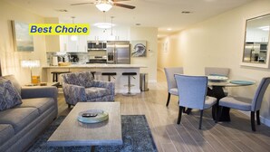 A modern living room with a sofa, armchair, coffee table, and a dining area with chairs and a table. - NewBestChoice🌴2pools,1Hot, Internet,Tennis🌞BeachSvc,2 Chair,1 Umbrella,Sleep 6 (Miramar Beach)
