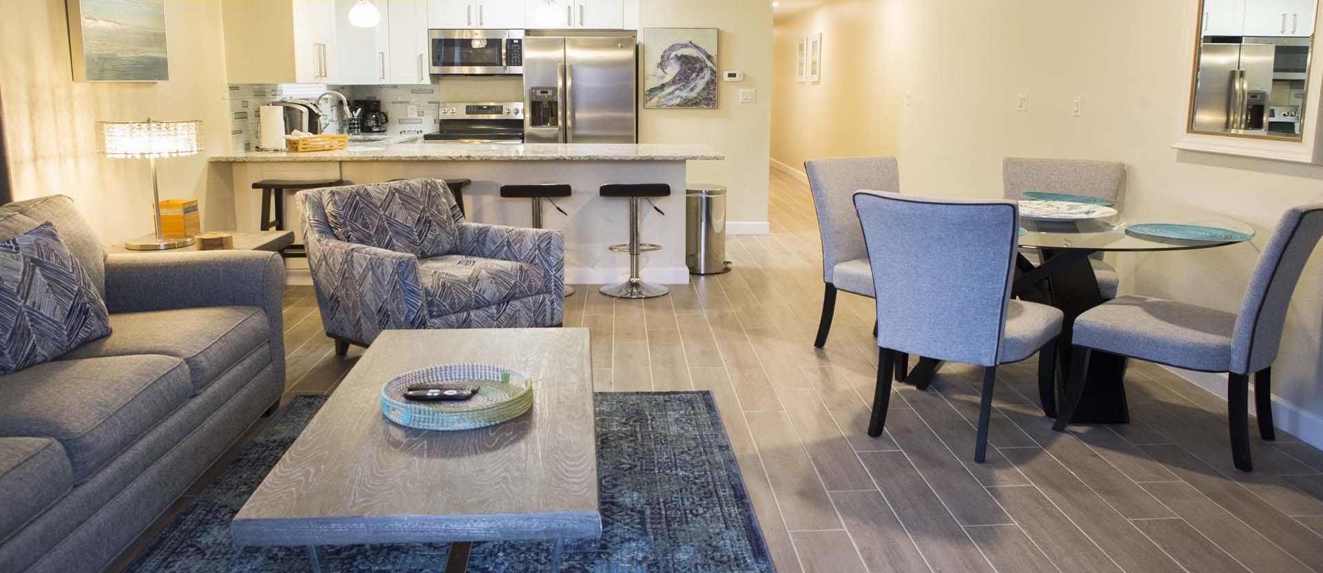 A modern living room with a sofa, armchair, coffee table, and a dining area with chairs and a table.