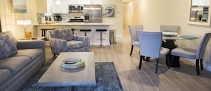 A modern living room with a sofa, armchair, coffee table, and a dining area with chairs and a table.