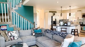 A modern living room with a grey sectional sofa, a coffee table, and a staircase with teal walls and wooden railings. - Calming Cabin Retreat (Outside North Harbour)