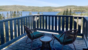 A wooden deck with two wicker chairs and a small table, overlooking a lake and forested hills. - Calming Cabin Retreat (Outside North Harbour)