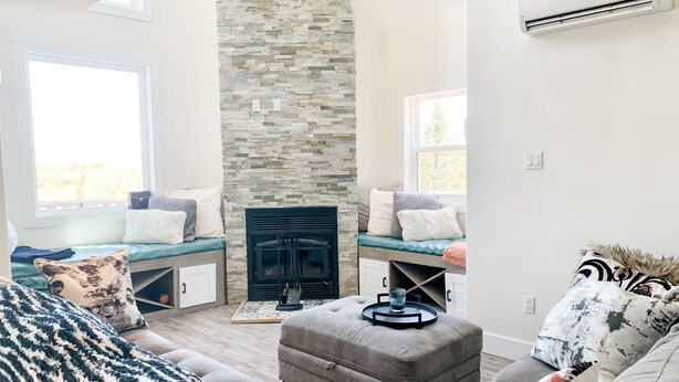 A living room with a stone fireplace, seating area, and large windows. - Calming Cabin Retreat (Outside North Harbour)
