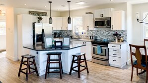 A modern kitchen with white cabinets, a central island with stools, stainless steel appliances, and pendant lighting. - Calming Cabin Retreat (Outside North Harbour)