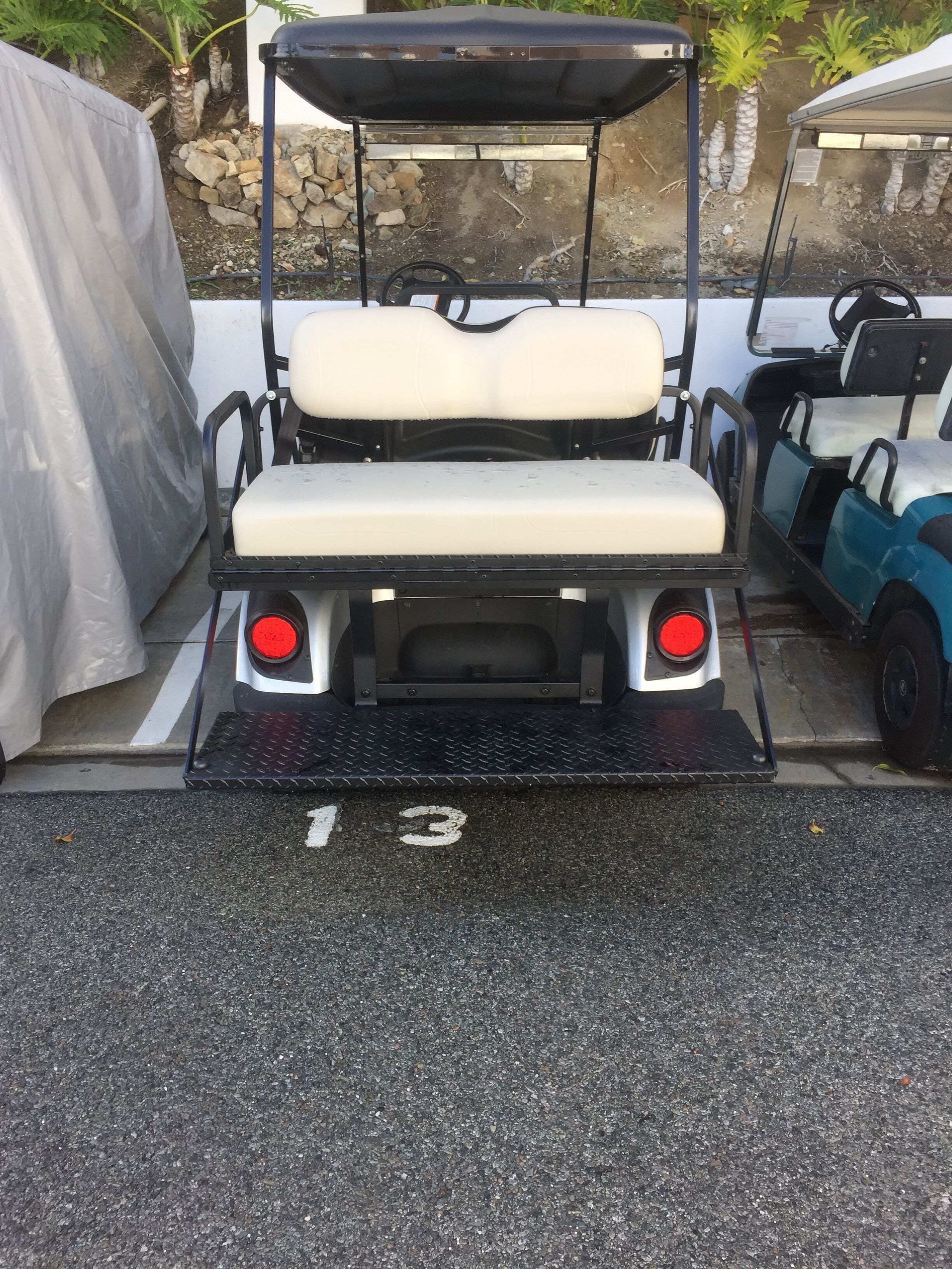 A golf cart with a black canopy, white seat, and red tail lights parked in a lot.