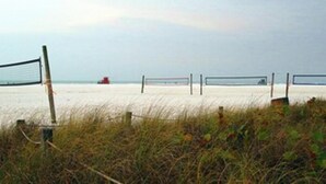 A beach volleyball net with a sandy beach and a red boat in the distance. - Jamaica Royale Siesta Key Condo 109 (Siesta Key)