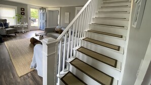 A spacious living area with a staircase, a sofa, a coffee table, and a view of the outdoors. - CLEAN, Walk To Beach, Ferries, Downtown, Newly Renovated House, Pet Friendly (Yarmouth)