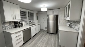 A modern kitchen with white cabinets, a stainless steel refrigerator, a dishwasher, and a coffee maker. - CLEAN, Walk To Beach, Ferries, Downtown, Newly Renovated House, Pet Friendly (Yarmouth)