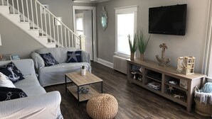 A living room with a staircase, a sofa, a coffee table, and a TV mounted on the wall. - CLEAN, Walk To Beach, Ferries, Downtown, Newly Renovated House, Pet Friendly (Yarmouth)