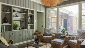 Una sala de estar acogedora con un gran ventanal, una estantería y muebles de mimbre.