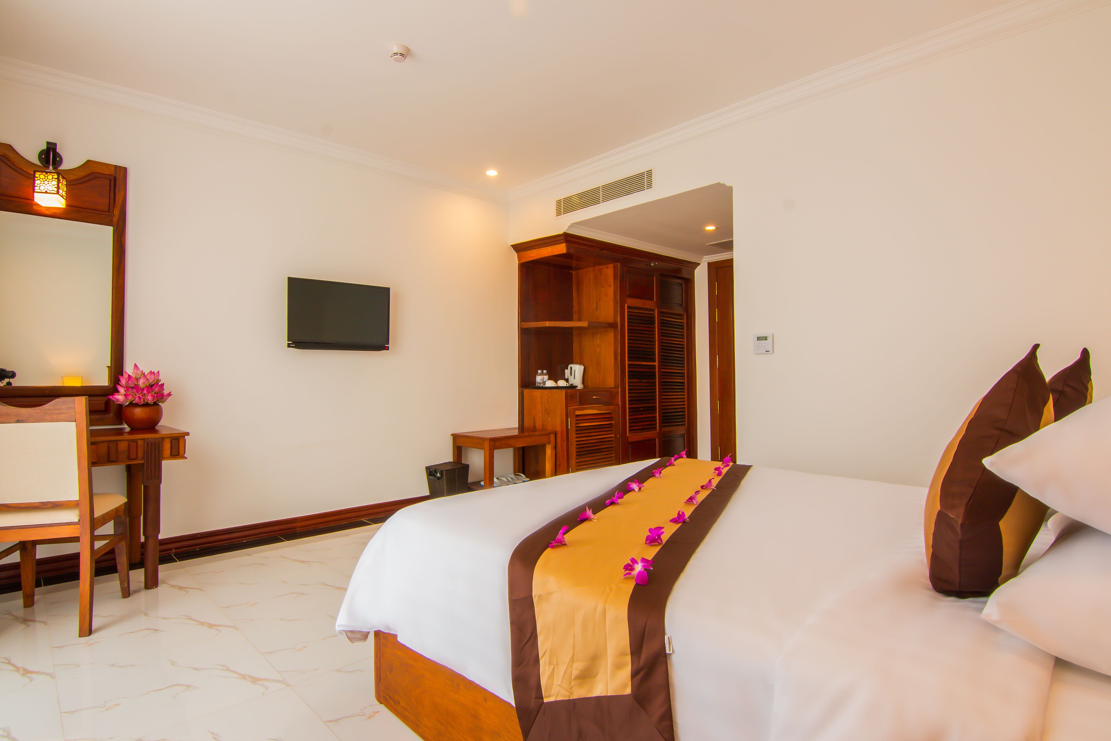 A hotel room with a bed, a desk, a chair, a TV, and a wardrobe.