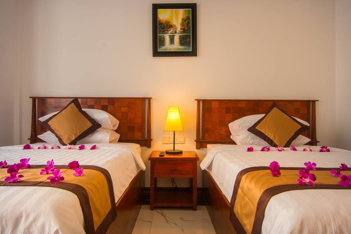 A hotel room with two beds, a nightstand with a lamp, and a painting on the wall.