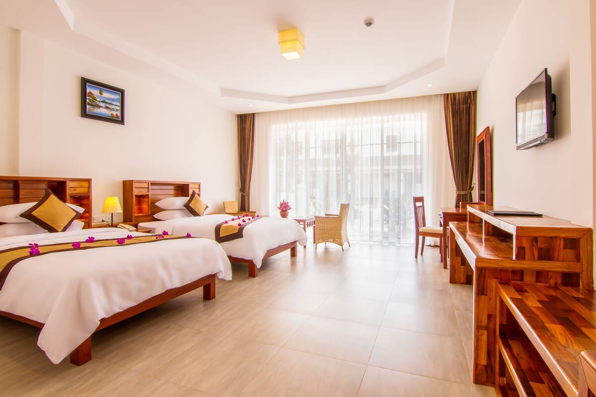 A hotel room with two beds, a desk, a chair, a TV, and a large window with curtains.