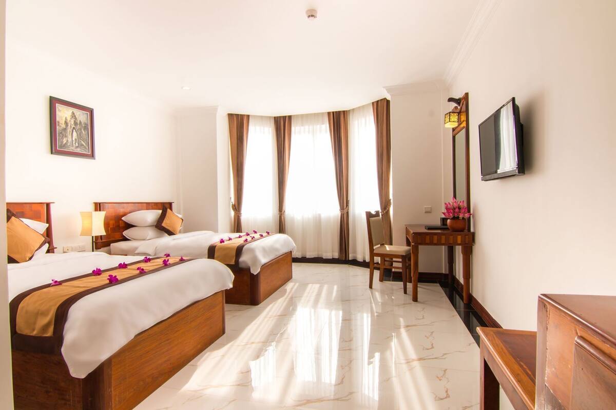 A hotel room with two beds, a desk, a chair, a TV, and a painting on the wall.