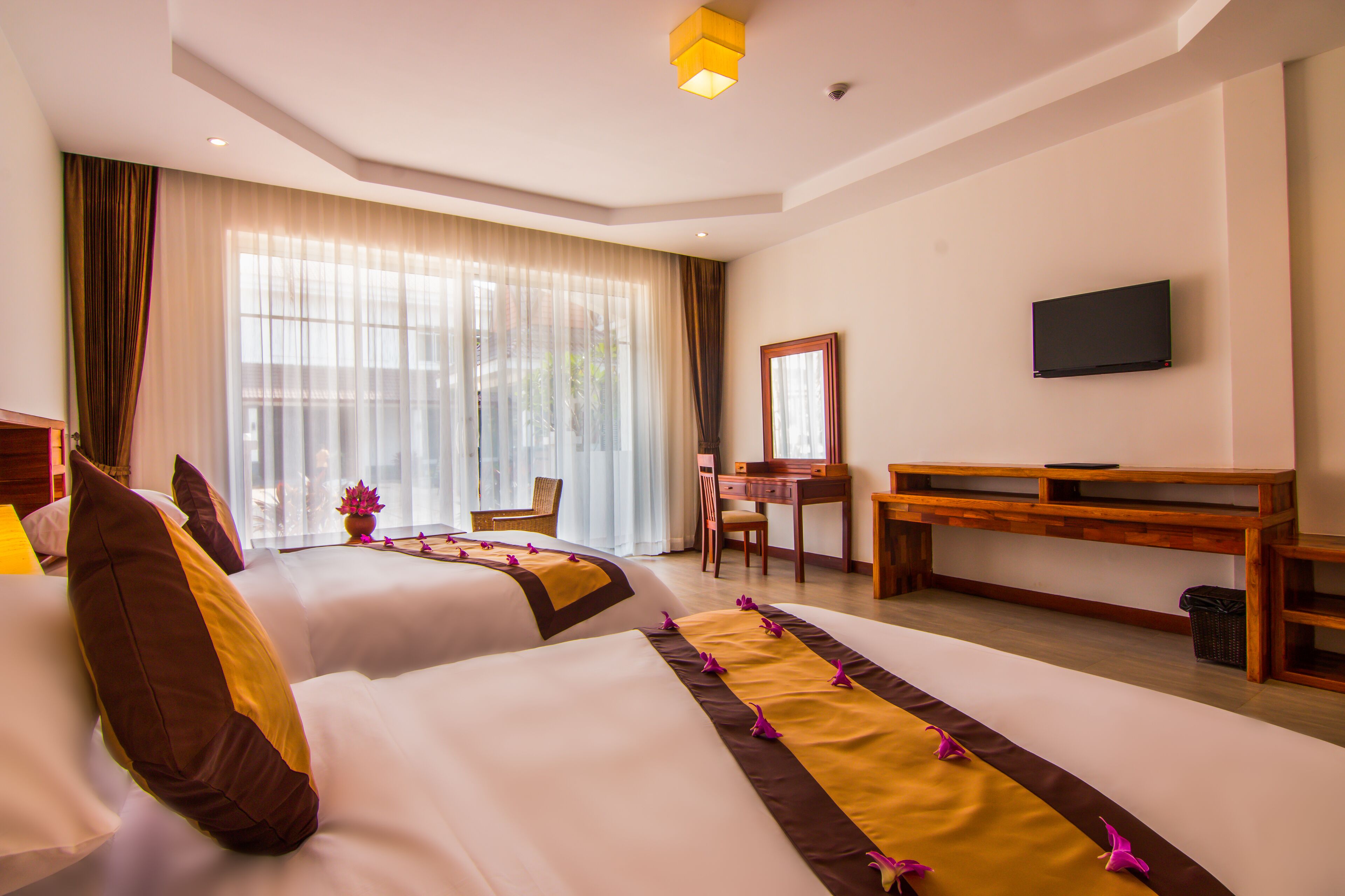 A hotel room with two beds, a desk, a chair, a television, and a large window with curtains.