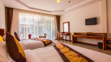 A hotel room with two beds, a desk, a chair, a television, and a large window with curtains.