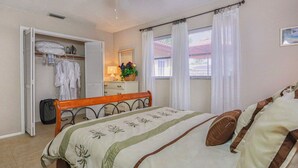 Ein Schlafzimmer mit Bett, Kleiderschrank, Spiegel und einem Fenster mit Vorhängen.