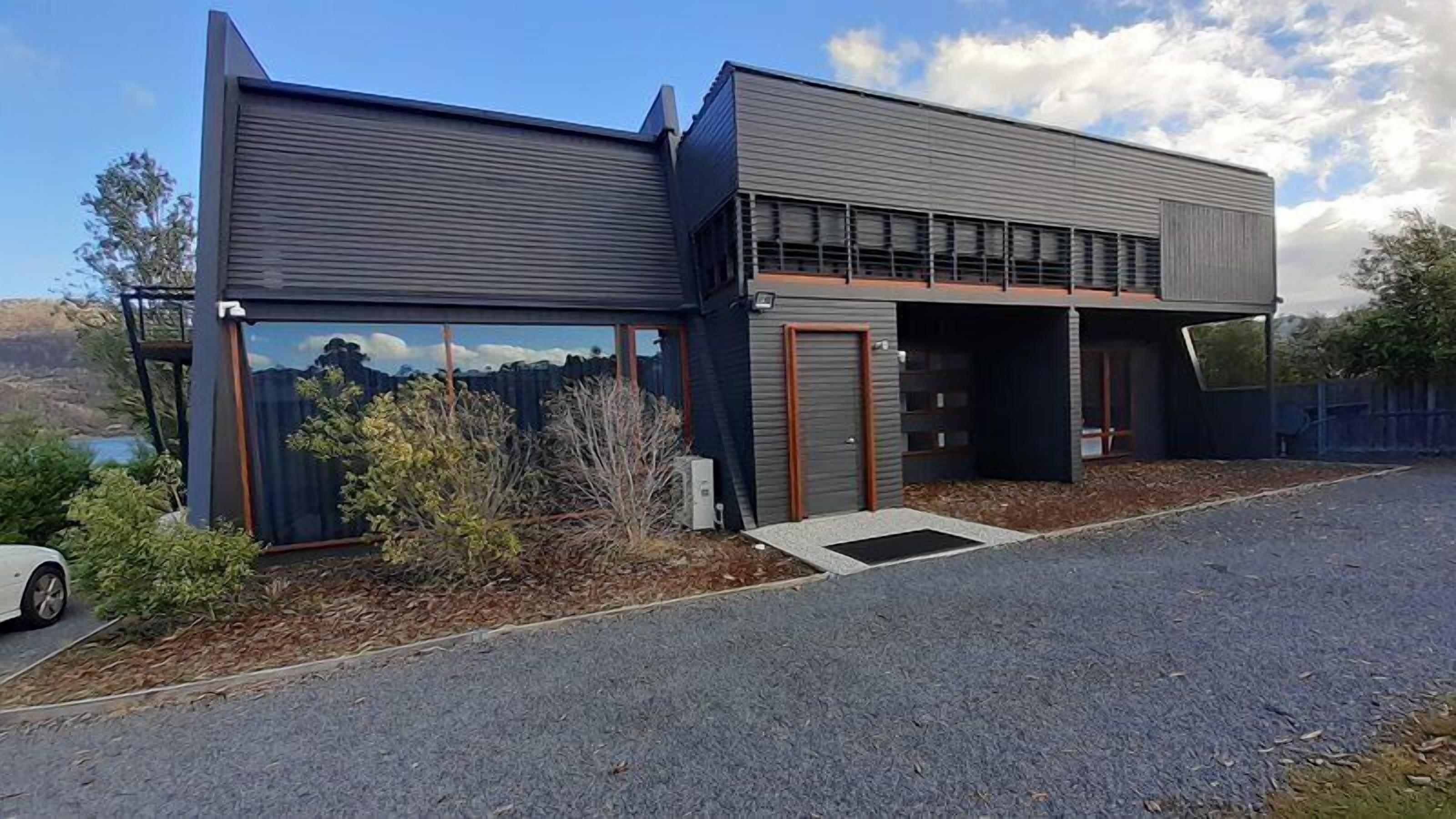 A modern two-story building with a garage, a covered driveway, and a view of a lake.