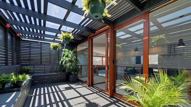 A modern outdoor deck with wooden flooring, glass doors, and potted plants. - Amazing Unique Five-Star Waterfront Retreat (Old Beach)