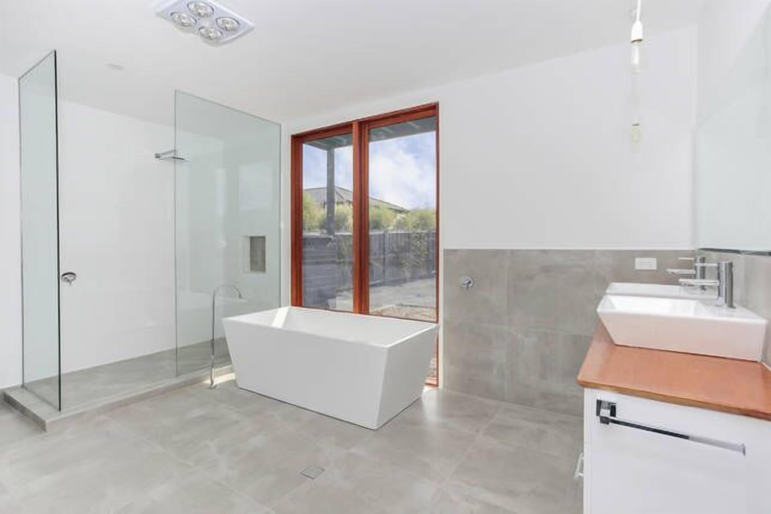 A modern bathroom with a glass shower enclosure, a freestanding bathtub, and a vanity with a wooden countertop.